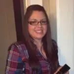 Woman with long dark hair and glasses wears a red plaid flannel and smiles for the camera