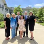 CCR Executives stand in a courtyard with a dark-haired woman in a white floral dress who holds two glass awards