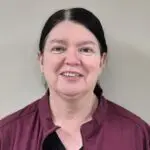 Woman with dark pulled back hair and a wine-colored zip-up smiles in front of a neutral background