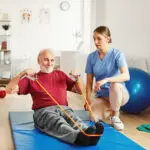 Doctor or nurse caregiver exercise with senior man at clinic or nursing home