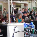Tables of elderly men and women sitting outdoors under a tent at an event