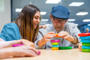 female nurse in blue scrubs helps elderly man in a blue cap stacking plastic rings at a table